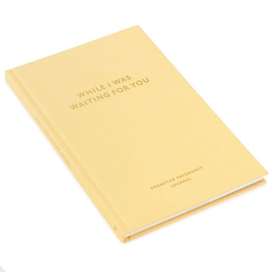While I Was Waiting Pregnancy Journal, hardcover, yellow cover with gold lettering, angled view.