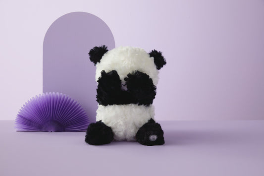 Peek-A-Boo Panda Stuffed Animal With Sound and Motion, 9", front view on a pastel purple background with decorative fan.