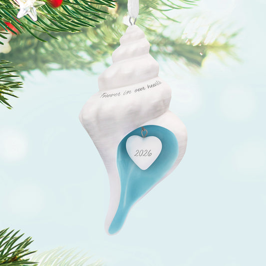 Forever in our hearts shell 2026, porcelain Christmas ornament featuring a white shell with sea-blue interior and year-dated heart charm.