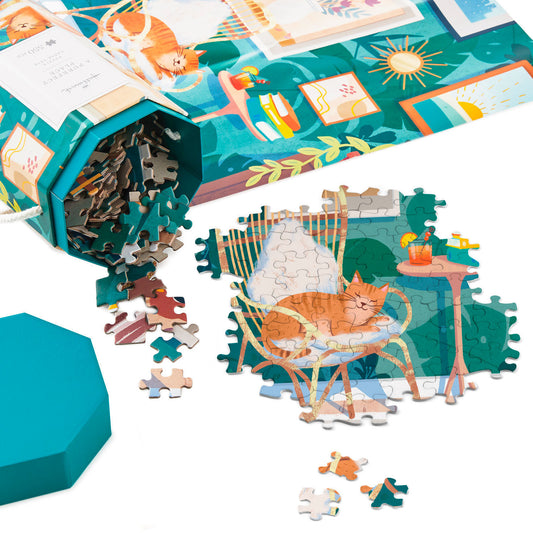 A Purrfect Place 550-Piece jigsaw puzzle (45.7cm x 61cm) displayed with pieces scattered and box in vibrant teal, featuring a cat in a cozy room.