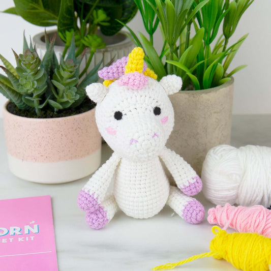 Unicorn DIY crochet kit with a cute plush unicorn beside pastel coloured wools and succulent plants in pots.