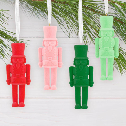 Signature Nutcracker, Set of 4 - Hallmark Christmas Ornament in red, pink, dark green, and light green with ribbon hangers on a festive backdrop.
