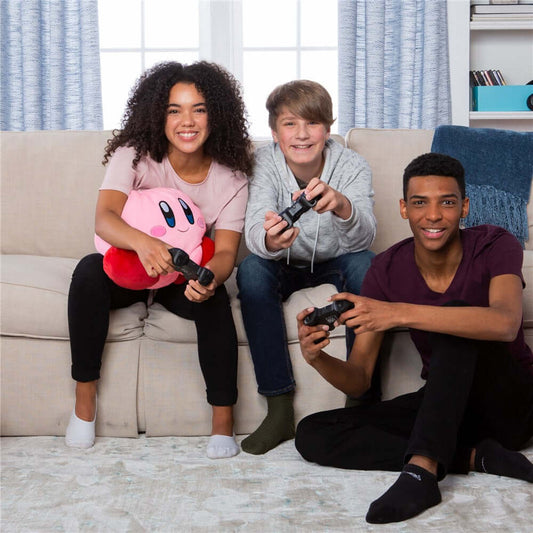 Kirby Mega Mocchi Mocchi Plush held by two kids in casual clothes sitting on a couch, gaming controllers in hand.