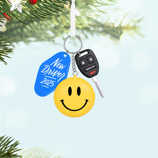 New Driver — 2025 Hallmark Keepsake Christmas Ornament, keychain design with a yellow smiley face and blue tag, hanging on a tree branch.