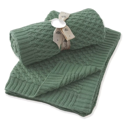 A set of sage green knit baby blankets, including a flat ribbed blanket and a waffle-knit rolled-up blanket tied with a beige ribbon, shown on a white background.