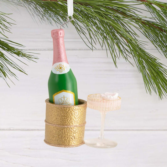 Signature Champagne - Hallmark Christmas Ornament featuring a green champagne bottle in a gold chiller with a glass and flower accent, flat lay.