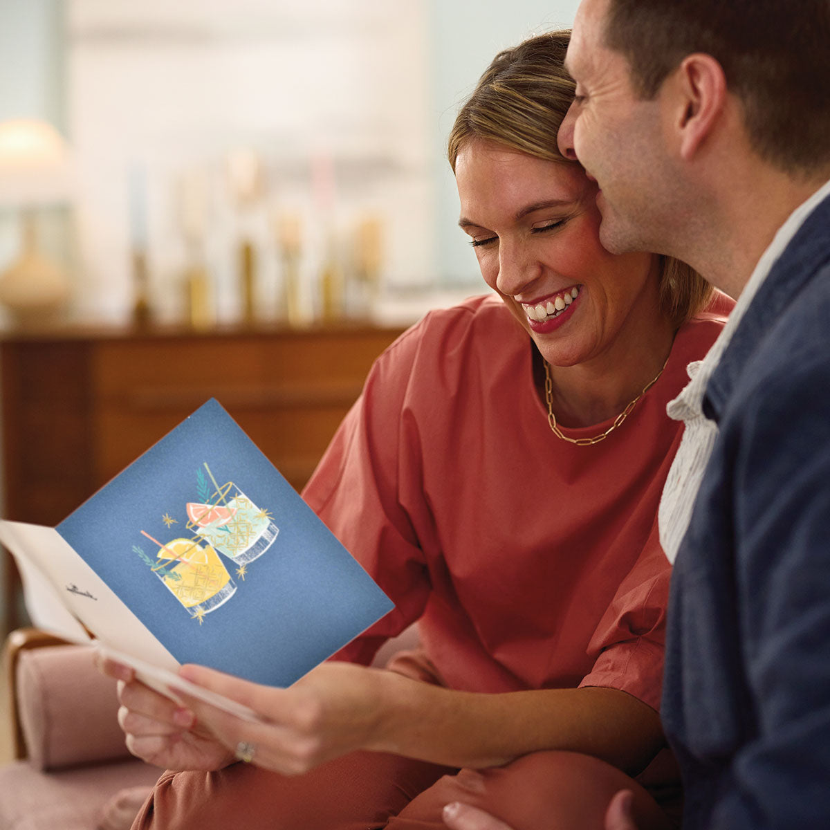 All greeting cards featuring a couple sharing a joyful moment while reading a colourful birthday card with cocktails illustration.