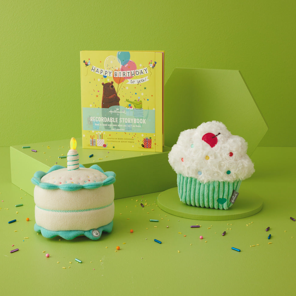 Two plush toys shaped like a cake and a cupcake with a birthday card on a green background