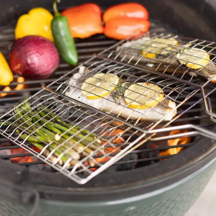 Barbecue grill basket with fish and vegetables grilling on a charcoal barbecue, featuring chrome finish and wooden handles.