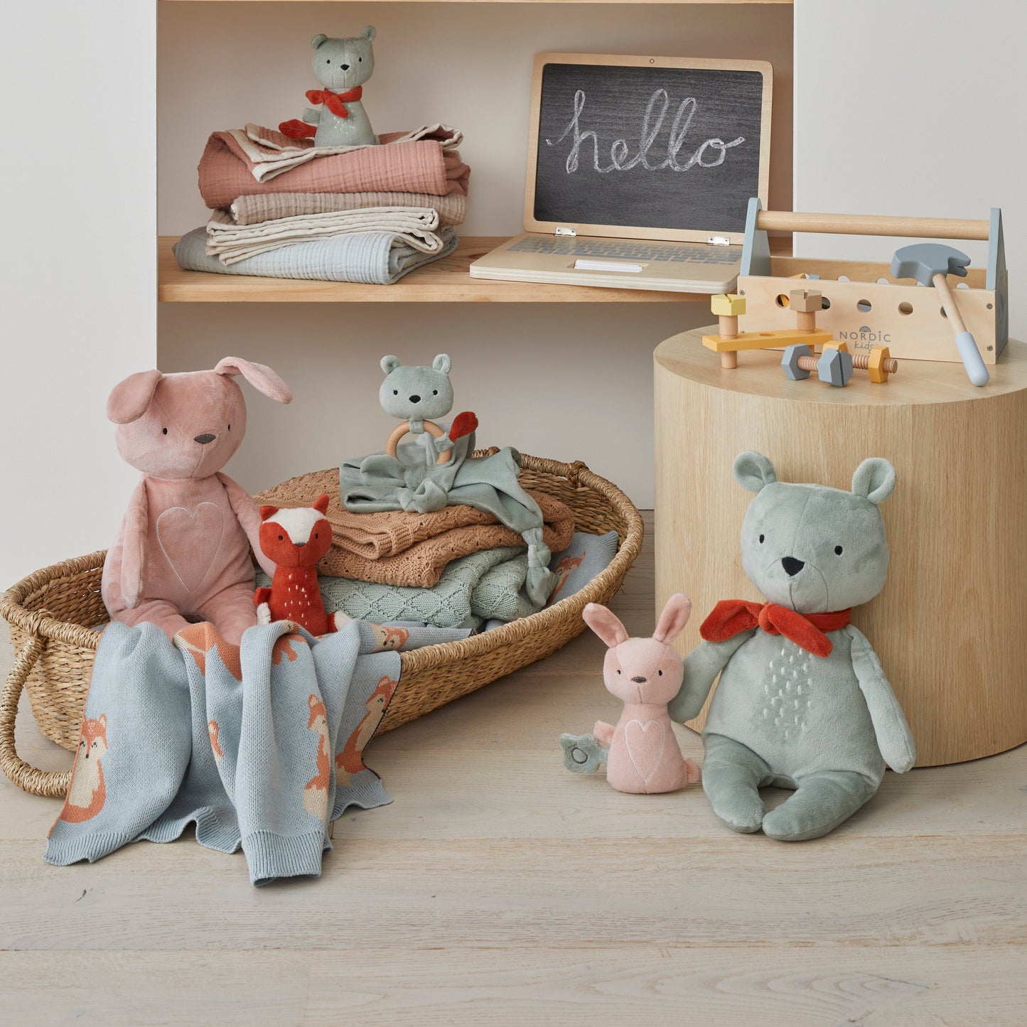 Freya plush bunny rattle surrounded by other plush toys and blankets in a vibrant display, ideal for playtime.