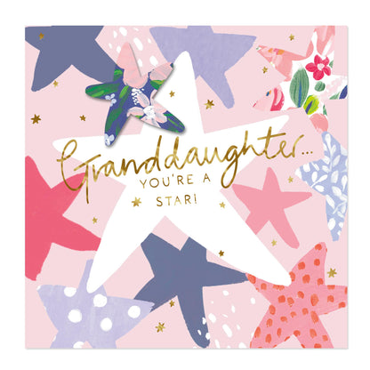 A square greeting card with a pink background and a collage of colorful starfish illustrations. A large white star in the center has the words 'Granddaughter.