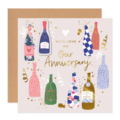 An anniversary greeting card with a kraft envelope behind it. The card has a light blush background and features illustrated champagne bottles in various colorful patterns, gold confetti, and the text 'WITH LOVE ON Our Anniversary' in gold script.