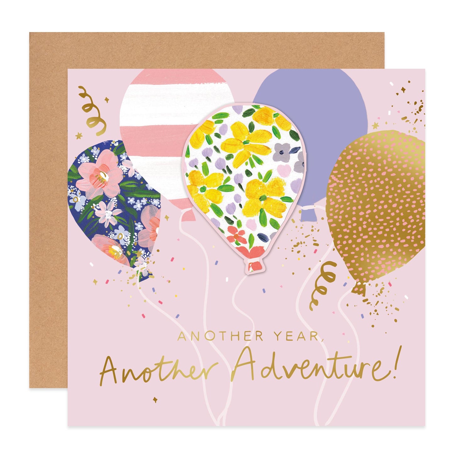 A square birthday card with a kraft envelope behind it. The card has a light pink background with illustrated balloons in floral and dotted patterns, gold confetti, and the text 'ANOTHER YEAR Another Adventure!' in gold script.