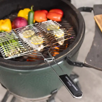 Barbecue grill basket with chrome finish, grilling vegetables on hot coals, featuring a wooden handle for easy lifting.