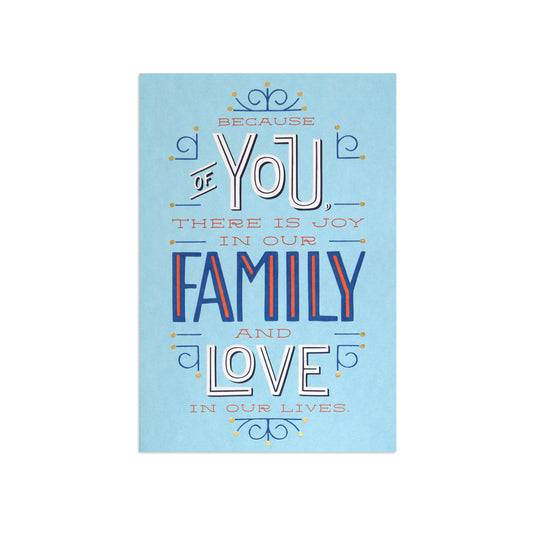 A square art print with a light blue background featuring a decorative typographic design that reads, 'BECAUSE OF YOU THERE IS JOY IN OUR FAMILY AND LOVE IN OUR LIVES.' The text uses white, navy blue, and orange-red lettering with small ornamental flourishes.