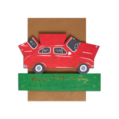 A handmade layered paper card featuring a red vintage car with its doors open, layered over a brown envelope-like backing and a green banner that reads 'Happy Father's Day thanks for always giving me the cold-shoulder.'.