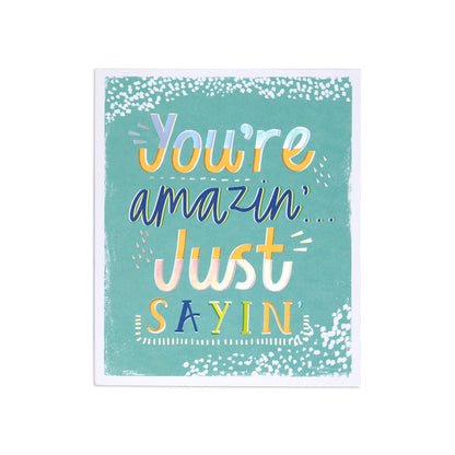 A square greeting card with a teal background and playful multicolor text reading 'You're amazin' Just SAYIN', shown on a plain white background.