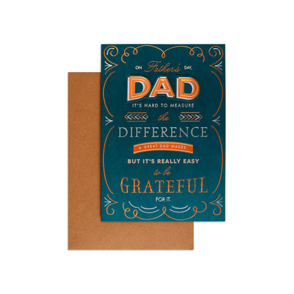 A Father's Day greeting card with a teal-blue background and orange and white decorative typography, shown with a brown envelope behind it on a light gray background.