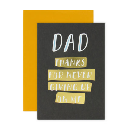 Hallmark Father's Day Card - Thanks For Never Giving Up On Me with gold foil accents and a yellow envelope, flat lay view.