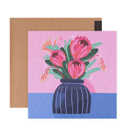 Hallmark x Christie Williams Gallery Blank Greeting Card - Pink Ice Proteas In Vase, featuring vibrant pink proteas in a dark vase, flat lay with beige envelope