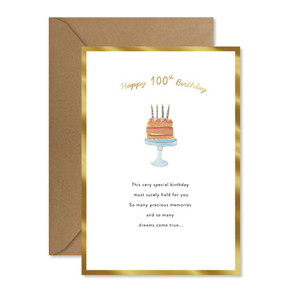 A 100th birthday greeting card with a gold foil border, featuring a watercolor cake illustration and a brown kraft envelope behind it on a white background.
