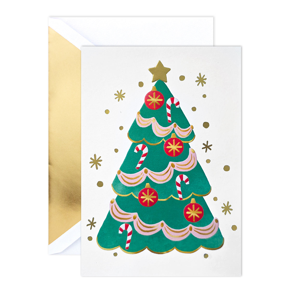 A Christmas greeting card with a gold envelope behind it. The card features an illustration of a green Christmas tree decorated with pink and white ribbons, red ornaments, candy canes, and gold stars on a white background.