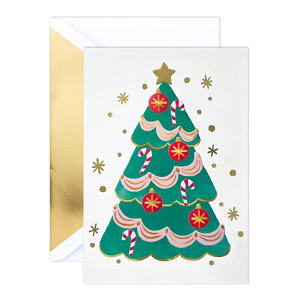 A Christmas greeting card with a gold envelope behind it. The card features an illustration of a green Christmas tree decorated with pink and white ribbons, red ornaments, candy canes, and gold stars on a white background.