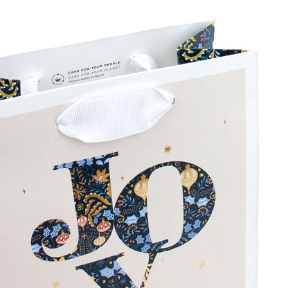 Hallmark Small Gift Bag - JOY featuring a detailed floral and bauble design with white grosgrain ribbon handles in an angled view.