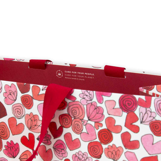 Hallmark x Love, Meredith Medium Gift Bag - Hearts & Flowers with red ribbon handles and heart illustrations, showcasing eco-friendly message.