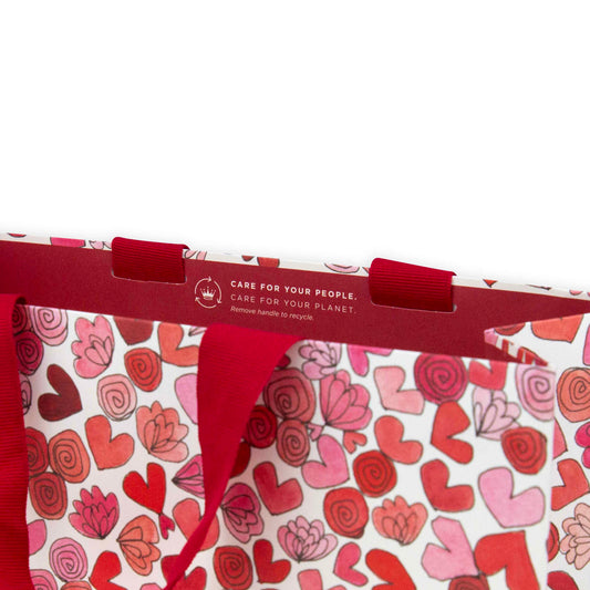 Hallmark x Love, Meredith Large Gift Bag - Hearts & Flowers featuring red grosgrain ribbon handles and pink and red heart illustrations, close up view.