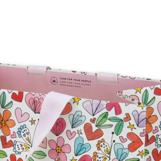 Hallmark x Love, Meredith Large Gift Bag - Butterflies, Hearts, Stars & Flowers with colourful floral and heart designs, showing pink grosgrain ribbon handles.