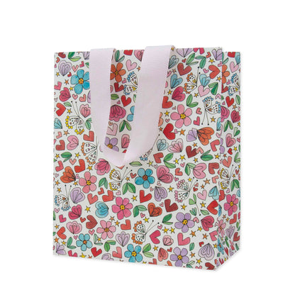 Hallmark x Love, Meredith Small Gift Bag - Butterflies, Hearts, Stars & Flowers with colourful floral and heart designs, showing light pink handles.