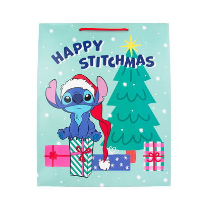 A light blue Christmas gift bag featuring Stitch wearing a Santa hat, with a green Christmas tree, presents, and the text 'HAPPY STITCHMAS' printed on it.