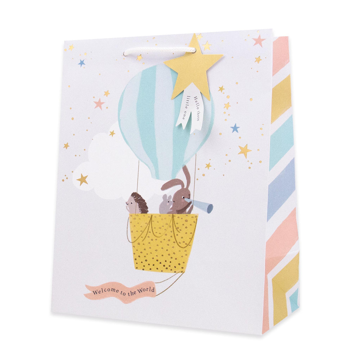 A white gift bag with a whimsical hot air balloon illustration featuring a bunny, hedgehog, and stars. The bag has a white handle, a gold star hanging tag, and pastel striped edges on the side.