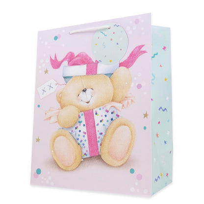 A pastel pink gift bag featuring a teddy bear illustration wearing a party hat and holding a wrapped gift, with confetti and polka dot details on a clean white background.