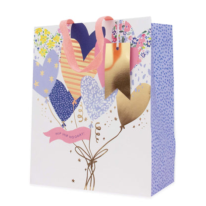 A decorative gift bag with a white front panel featuring a balloon bouquet illustration in pastel colors, pink ribbon handles, and a blue dotted side panel. The front reads 'HIP HIP HOOKAY!'.