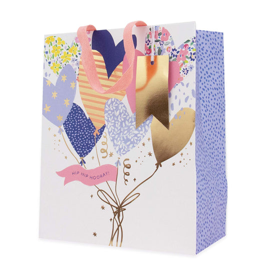 A decorative gift bag with a white front panel featuring a balloon bouquet illustration in pastel colors, pink ribbon handles, and a blue dotted side panel. The front reads 'HIP HIP HOOKAY!'.