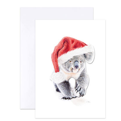 A white greeting card featuring a detailed illustration of a koala wearing a red Santa hat with white trim, shown with a white envelope behind it on a light gray background.