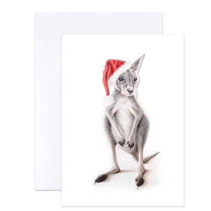 A greeting card featuring a detailed pencil-style illustration of a kangaroo wearing a red Santa hat, shown with a white envelope behind it on a light gray background.