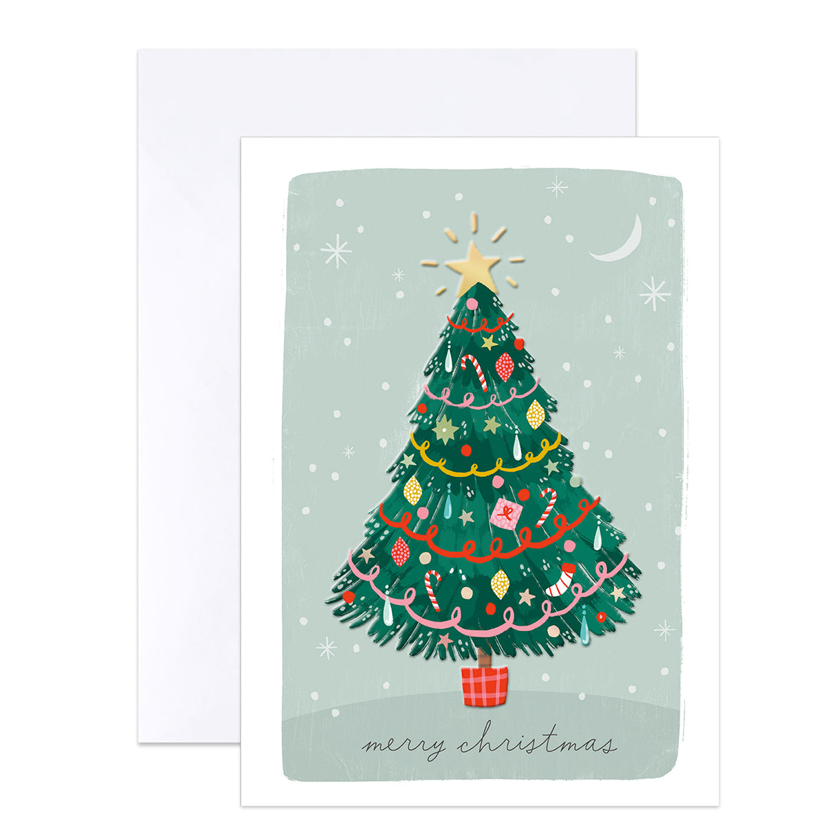 A Christmas greeting card with a white envelope behind it. The card features an illustration of a decorated green Christmas tree with ornaments, a gold star, a crescent moon, and the text 'merry christmas' at the bottom.