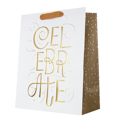 A white paper gift bag with a brown handle and a metallic gold foil script reading 'CELEBRATE' on the front. The side of the bag is brown with small white speckled confetti details, set against a plain white background.