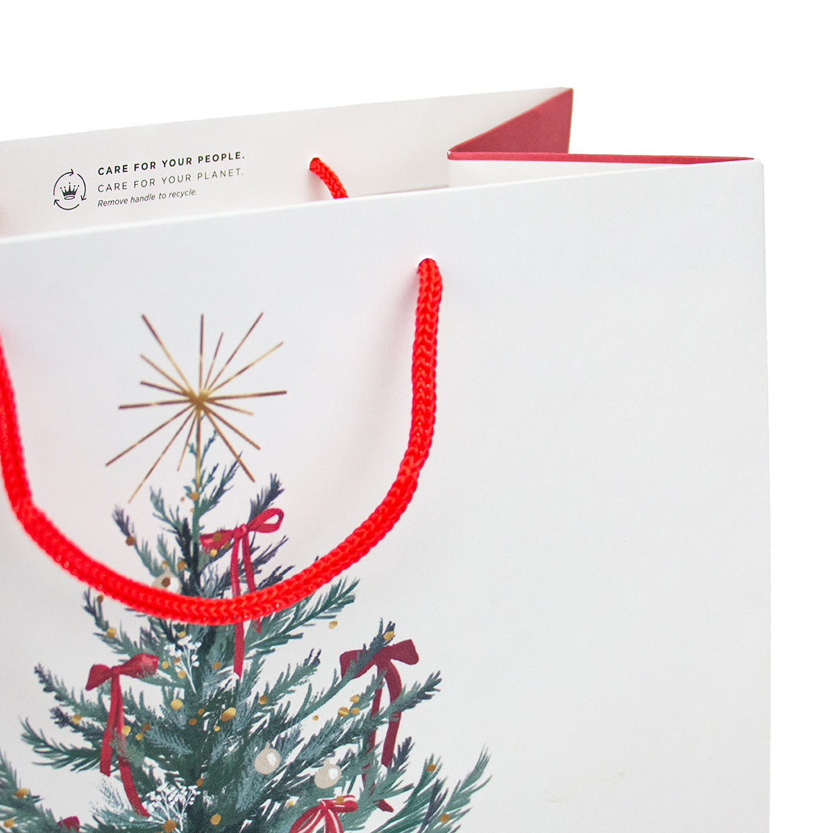 A white paper gift bag with red rope handles, featuring a printed Christmas tree illustration with red bows and a gold star topper. The bag has a visible 'CARE FOR YOUR PEOPLE.