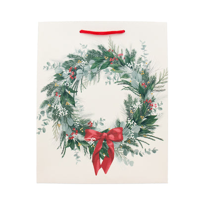 An off-white paper gift bag featuring a watercolor-style Christmas wreath design with green foliage, red berries, and a red bow, complete with a red hanging loop at the top.