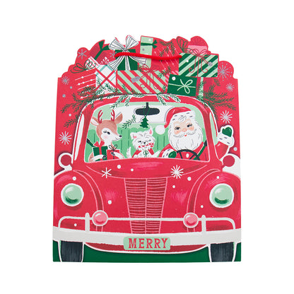 A festive Christmas-themed gift bag shaped like a red vintage car, decorated with Santa Claus, a reindeer, a cat, wrapped presents, pine branches, and the word 'MERRY' on the front, shown on a plain white background.