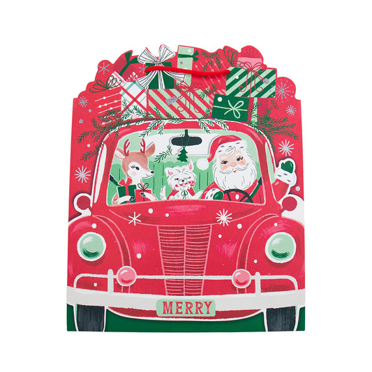 A festive Christmas-themed gift bag shaped like a red vintage car, decorated with Santa Claus, a reindeer, a cat, wrapped presents, pine branches, and the word 'MERRY' on the front, shown on a plain white background.
