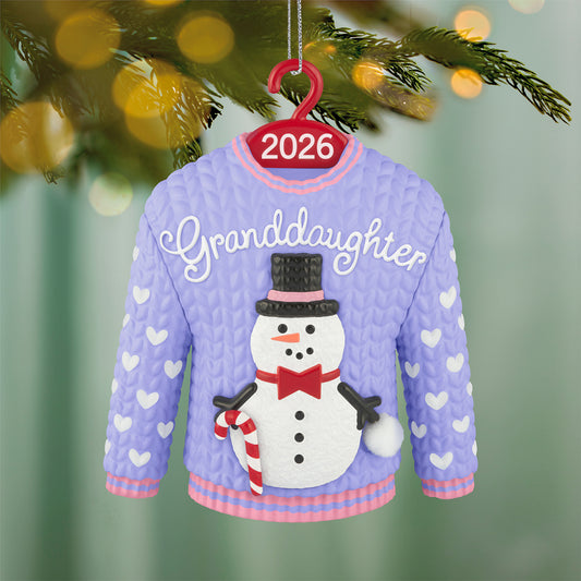 Granddaughter Snowman Sweater 2026 — 2026 Hallmark Keepsake Christmas Ornament, purple and pink design featuring a snowman and hearts, hanging on a tree.