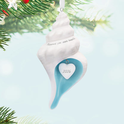 Forever in our hearts shell 2026, porcelain Christmas ornament featuring a white shell with sea-blue interior and year-dated heart charm.