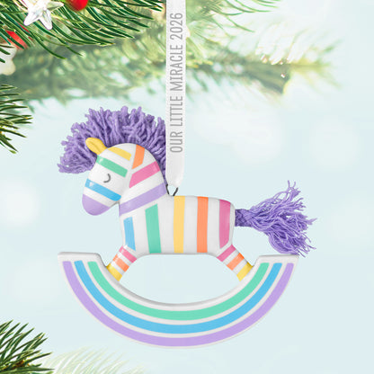 Our Little Miracle 2026 porcelain and fabric ornament featuring a pastel rocking horse design with a lavender mane, suspended from a Christmas tree.