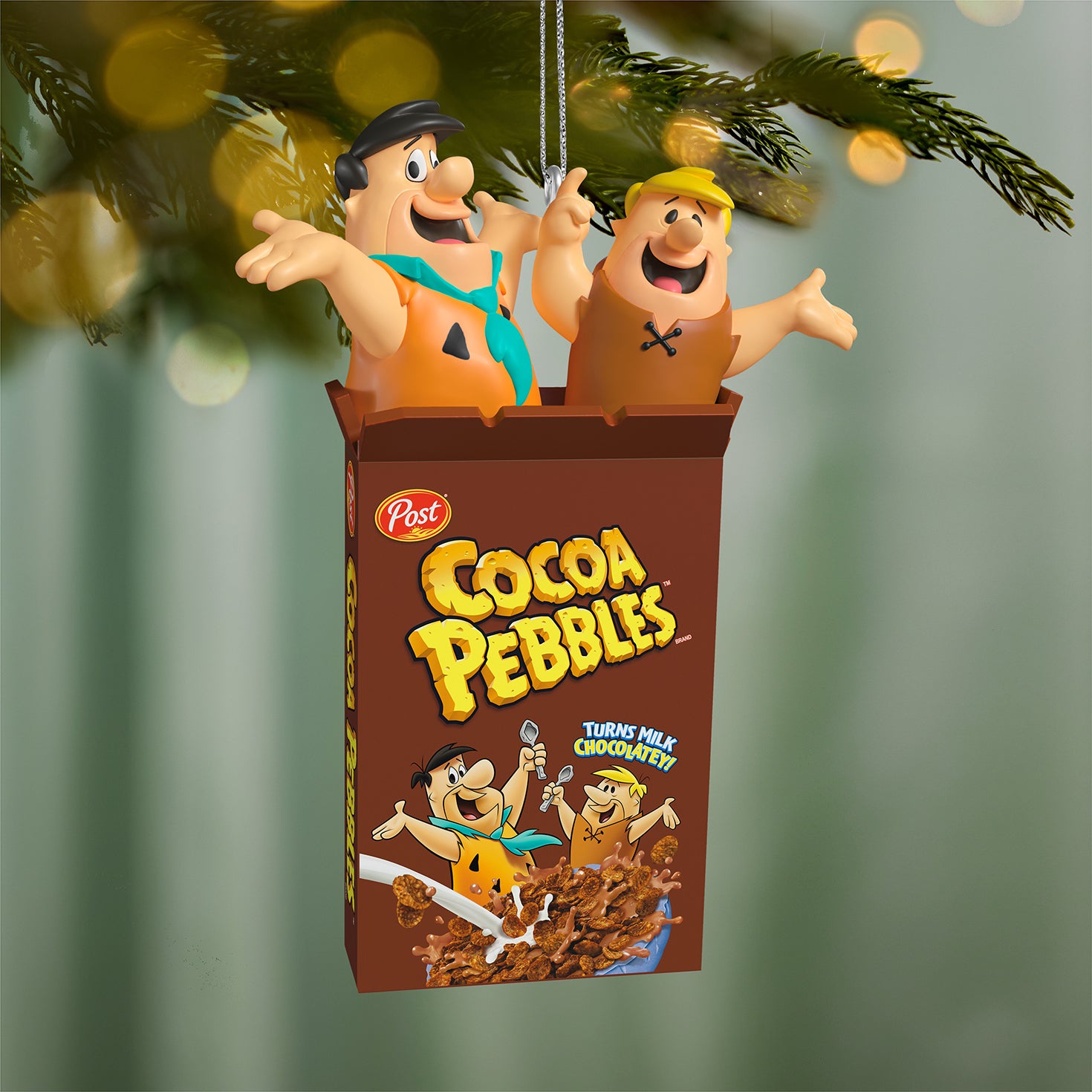 The Flintstones™ Cocoa Pebbles — 2026 Hallmark Keepsake Christmas Ornament featuring Fred and Barney bursting from a cereal box, hanging on a Christmas tree.