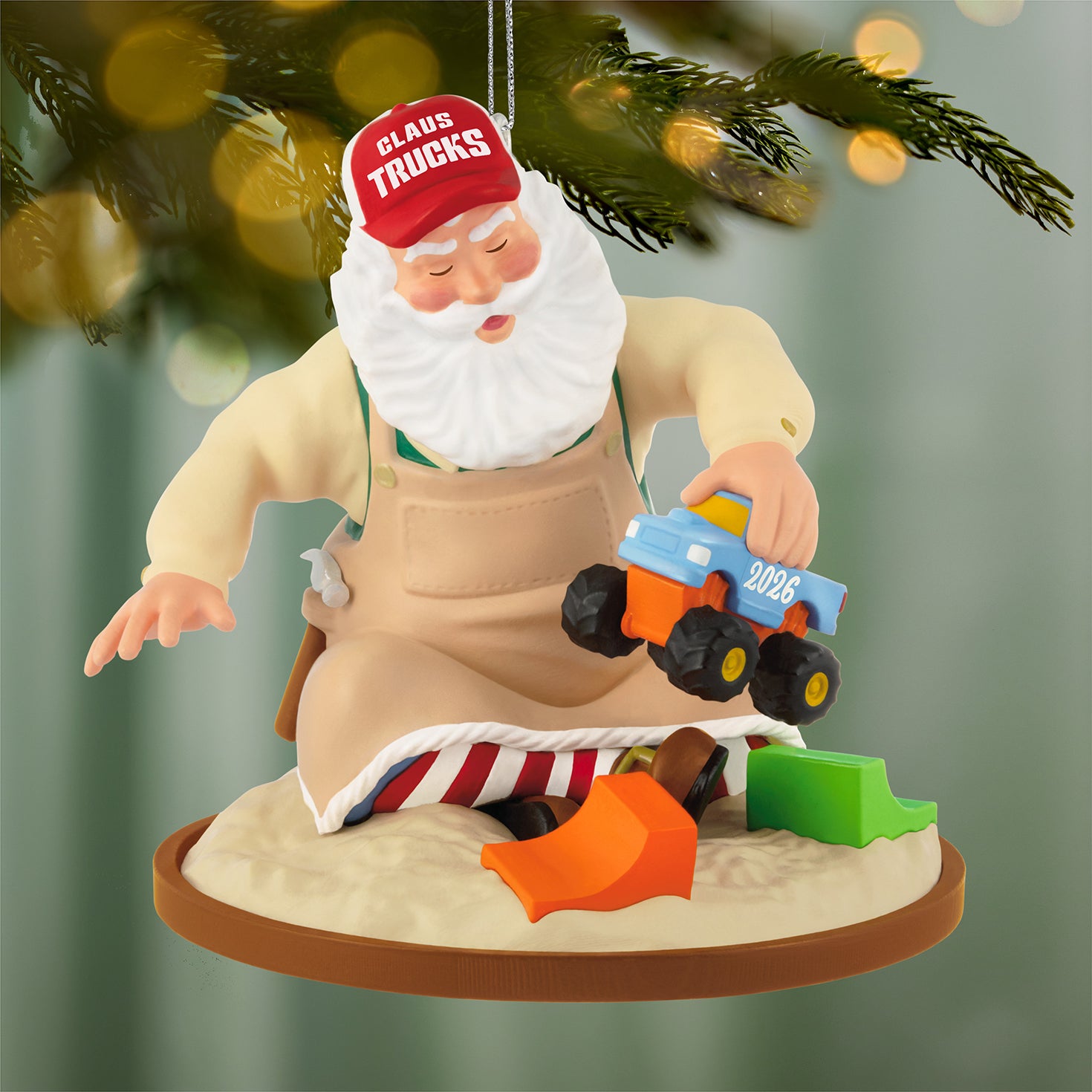 Toymaker Santa, 27th in the Series — 2026 Hallmark Keepsake Christmas Ornament, dressed in workshop apron and trucker hat, testing a monster truck in sand.
